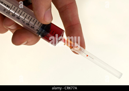 Vista di un ago fissato ad una siringa, la punta dell'ago contiene una gocciolina di liquido. Foto Stock