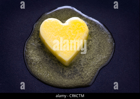 Un cuore di burro a forma di pat fusione su una superficie antiaderente dieta sana nozione Foto Stock