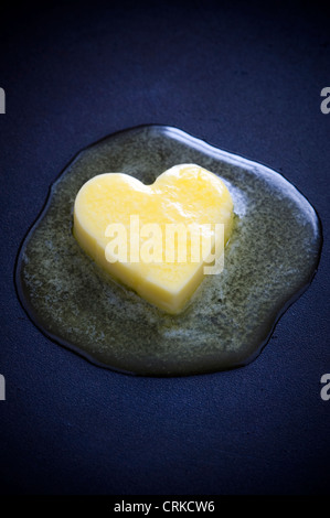 Un cuore di burro a forma di pat fusione su una superficie antiaderente che rappresenta un cuore sano concetto Foto Stock