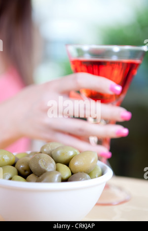 Vicino sul vaso di olive verdi davanti a una donna di mano in mano un bicchiere di rosso Campari Foto Stock