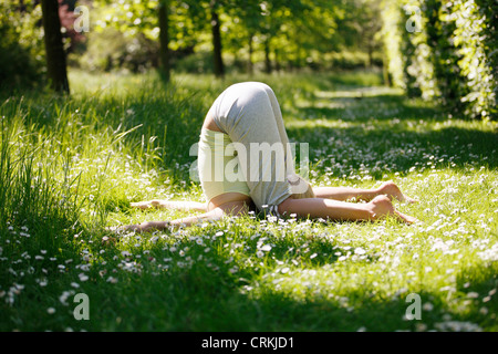 Una giovane donna a praticare yoga al di fuori, pressione auricolare pongono Foto Stock