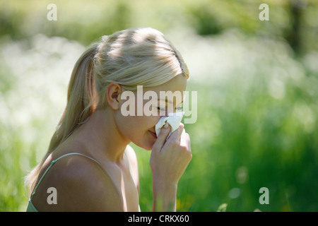 Una giovane donna bionda di starnuti ripetuti in un tessuto Foto Stock