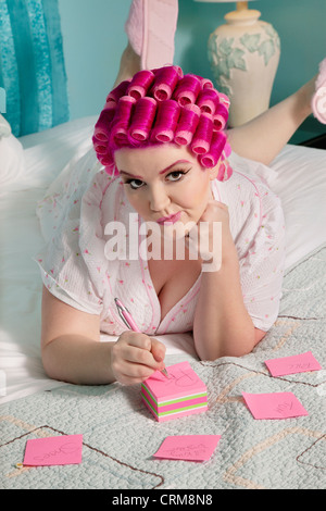 Ritratto di giovane donna sdraiata sul letto durante la scrittura su quaderni appiccicoso Foto Stock