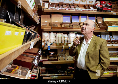 Piccolo negozio di tabacco proprietario guardando le scatole di sigari sul display in negozio Foto Stock