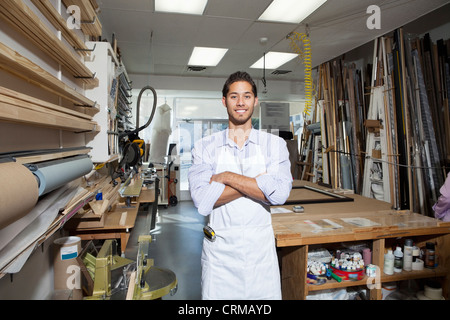 Ritratto di un felice giovane artigiano in piedi con le braccia incrociate in officina Foto Stock