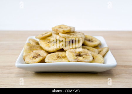 Banane essiccate chip sul tagliere di legno contro uno sfondo bianco Foto Stock