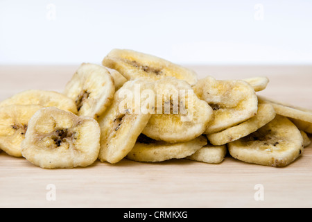 Banane essiccate chip sul tagliere di legno contro uno sfondo bianco Foto Stock