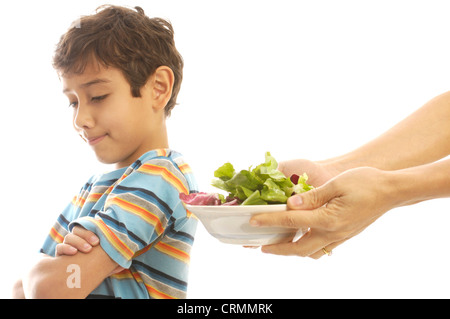 Un giovane ragazzo che rifiuta di mangiare una ciotola di insalata, dato a lui da sua madre Foto Stock