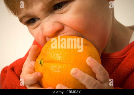 Un giovane bambino mordere nella pelle amaro di un arancione. Foto Stock