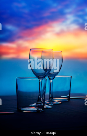 Piatto di bicchieri di cristallo e vetri trasparenti su un tramonto sul mare tabella Foto Stock