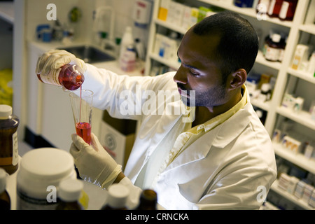 Un farmacista riversa in rosso di un liquido in un cilindro graduato. Foto Stock