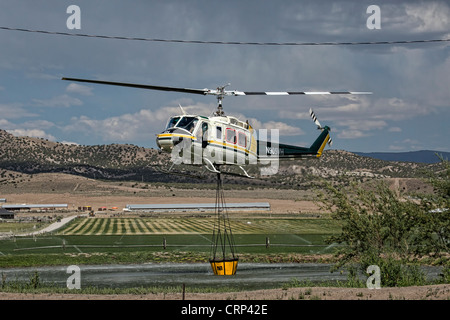 Elicottero foresta di antenna di combattimento aereo della benna di riempimento con acqua dal laghetto per caduta sulle fiamme e hot spot. Foto Stock