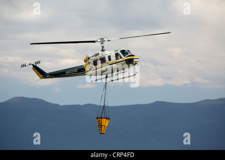 Elicottero foresta di antenna di combattimento aereo della benna di riempimento con acqua dal laghetto per caduta sulle fiamme e hot spot. Foto Stock