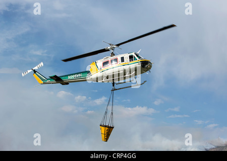 Elicottero foresta di antenna di combattimento aereo della benna di riempimento con acqua dal laghetto per caduta sulle fiamme e hot spot. Foto Stock