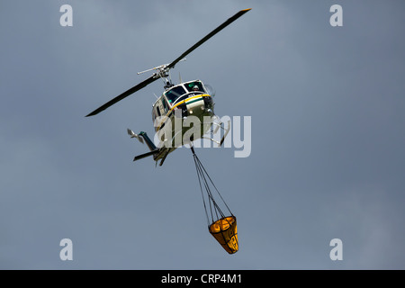 Elicottero foresta di antenna di combattimento aereo della benna di riempimento con acqua dal laghetto per caduta sulle fiamme e hot spot. Foto Stock