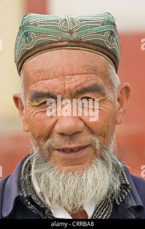 Un anziano Uyghur uomo cinese pongono per la fotocamera in abiti tradizionali al mercato locale nella piccola cittadina di Upal, Cina. Foto Stock