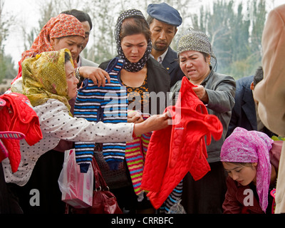 Uyghur le donne cinesi acquistare vestiti per bambini al mercato locale nella piccola cittadina di Upal, Cina. Foto Stock