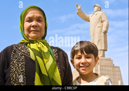 Un Uyghur madre cinese e il suo bambino rappresenta per la fotocamera con la statua di Mao Zedong dietro a Kashgar. Foto Stock
