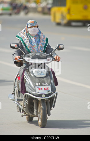 Un Cinese Uyghur donna viaggia lungo una strada sul suo scooter a Kashgar. Foto Stock