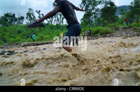 Un uomo le lotte per guadare attraverso una strada allagata durante la stagione dei monsoni in Nepal. Foto Stock