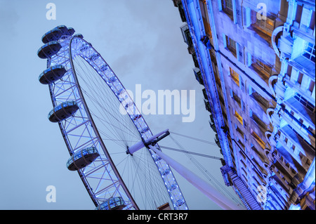 Il London Eye al crepuscolo con edifici. Il London Eye (precedentemente noto come il Millennium Wheel) al crepuscolo contro un cielo nuvoloso. Foto Stock