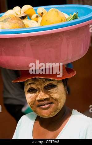 Donna con la faccia la vernice per la vendita di frutta, Mahajanga, Madagascar Foto Stock