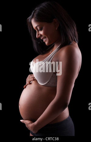 Giovane bella indiana incinta di toccare la sua pancia, su sfondo nero Foto Stock