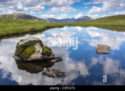 Riflessioni del cielo in un tarn a testa Gillercomb, Brandreth nel distretto del lago. Kirk cadde e il pilastro sono in distanza. Foto Stock