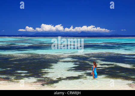 Donna in blu sarong wades nelle acque in prossimità di Anse Source d'Argent su La Digue alle Seychelles Foto Stock