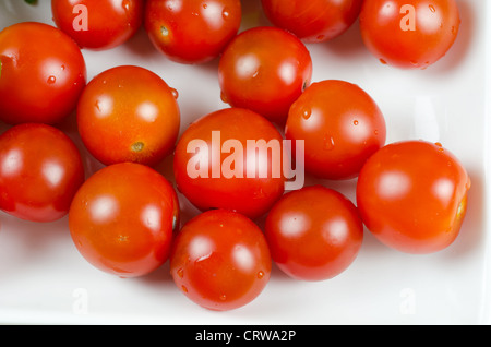 Pomodori ciliegia in corrispondenza della piastra su bianco Foto Stock