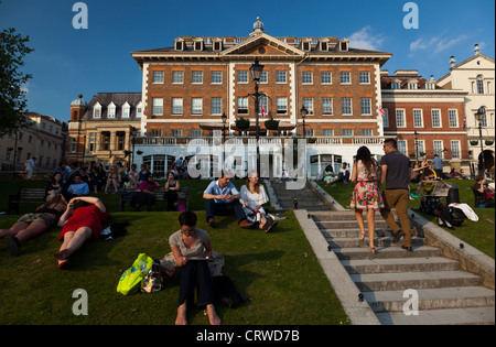 La gente seduta all aperto nei pomeriggi estivi sulla striscia erbosa al riverfront in Richmond a Londra. Foto Stock