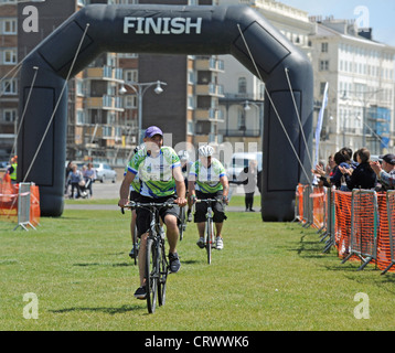 Cyclists cross the finishing line in Hove after completing the Capital to Coast Cycle ride from London to Brighton and Hove 2012 Foto Stock