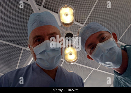 Un paziente dal punto di vista di un team di chirurghi mascherato sotto le luci in un ospedale teatro operativo. Foto Stock