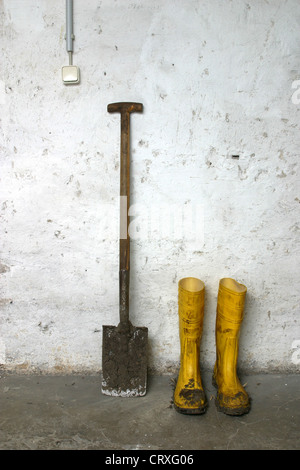 Wellies e una vanga su una parete basale Foto Stock