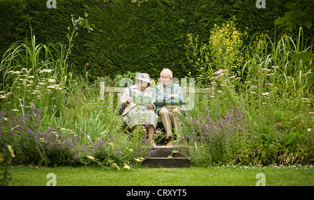 Anziana coppia caucasica sedette su panca di legno in giardino guardando la lettura di un foglietto Foto Stock