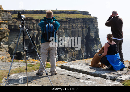 Gli amanti del birdwatching con il binocolo e un telescopio per guardare i puffini e colonie di uccelli marini nidificazione sugli scogli. Testa Noup Westray Isole Orcadi Scozia UK Foto Stock