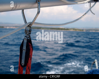 Barca a vela boom con raccordi in mare e sulla costa a distanza Foto Stock