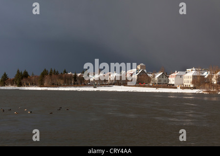 Le case e gli edifici confinanti con lo stagno, Reykjavik, Islanda, sotto una tempesta cielo grigio Foto Stock