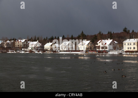 Le case e gli edifici confinanti con lo stagno, Reykjavik, Islanda, sotto una tempesta cielo grigio Foto Stock