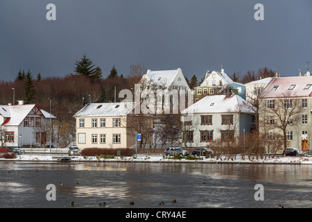 Le case e gli edifici confinanti con lo stagno, Reykjavik, Islanda, sotto una tempesta cielo grigio Foto Stock