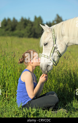 Ragazza seduta in un prato mentre la bacia pony Foto Stock