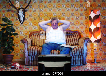 Un uomo grasso seduta sul divano e infastidisce se stesso Foto Stock