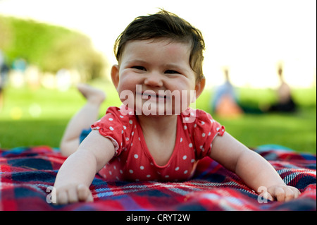 Sorridenti Baby girl (6 mesi) sul tappetino picnic sull'erba nel parco con la pancia del tempo Foto Stock