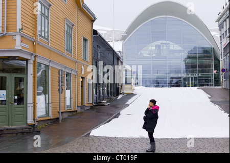 Donna locale utilizzando il telefono cellulare nella scena di strada dalla moderna libreria Biblioteket in Tromsoya, Tromso, nel nord della Norvegia Foto Stock