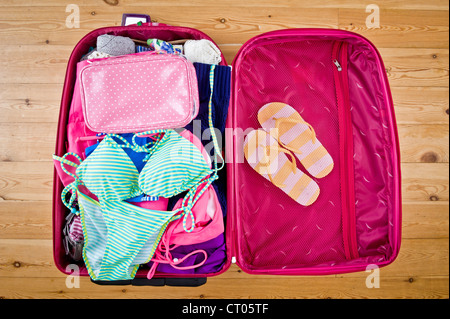 Valigia rosa aperta con bikini e infradito pronti per una vacanza al sole Foto Stock