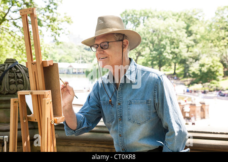 Un maschio maturo pittore che lavora su un cavalletto, al Central Park di New York Foto Stock