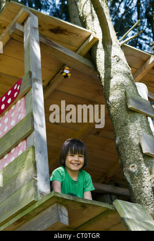 Sorridente ragazzo seduto in casa ad albero Foto Stock