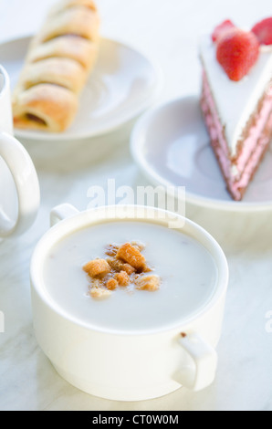 Zuppa di funghi con pane tostato, torta di fragole e tè come sfondo, naturale luce del sole di mattina. Foto Stock