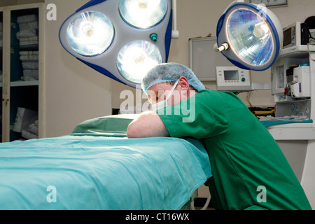 Una stanca oltre lavorato chirurgo stabilisce a poggiare su un tavolo operatorio. Foto Stock