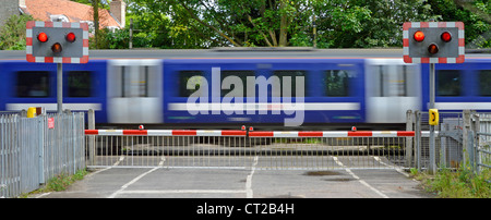 I binari ferroviari rosso lampeggiante spia livello di segno attraversando i cancelli di barriera stradale del paese treni passeggeri motion blur a Margaretting Essex England Regno Unito Foto Stock